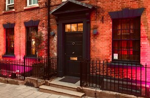 A brick building with a black front door, a small porch, and a black metal fence. - The Silk House (Leek)