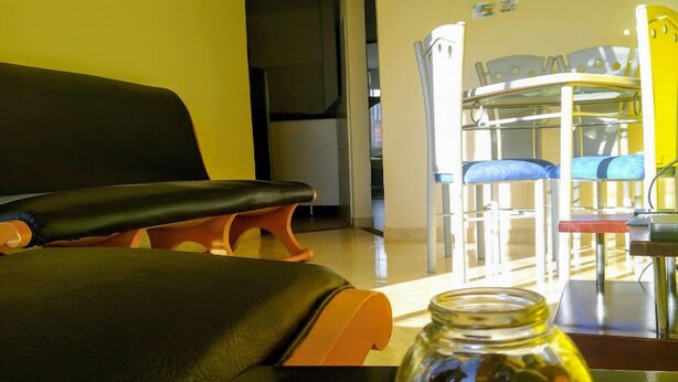 Una habitación con un sofá negro, una mesita con un tarro de cristal y un comedor con sillas y una mesa.