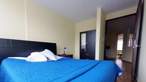 Habitación de hotel con cama, mesita de noche, escritorio, armario y baño visible a través de una puerta abierta.