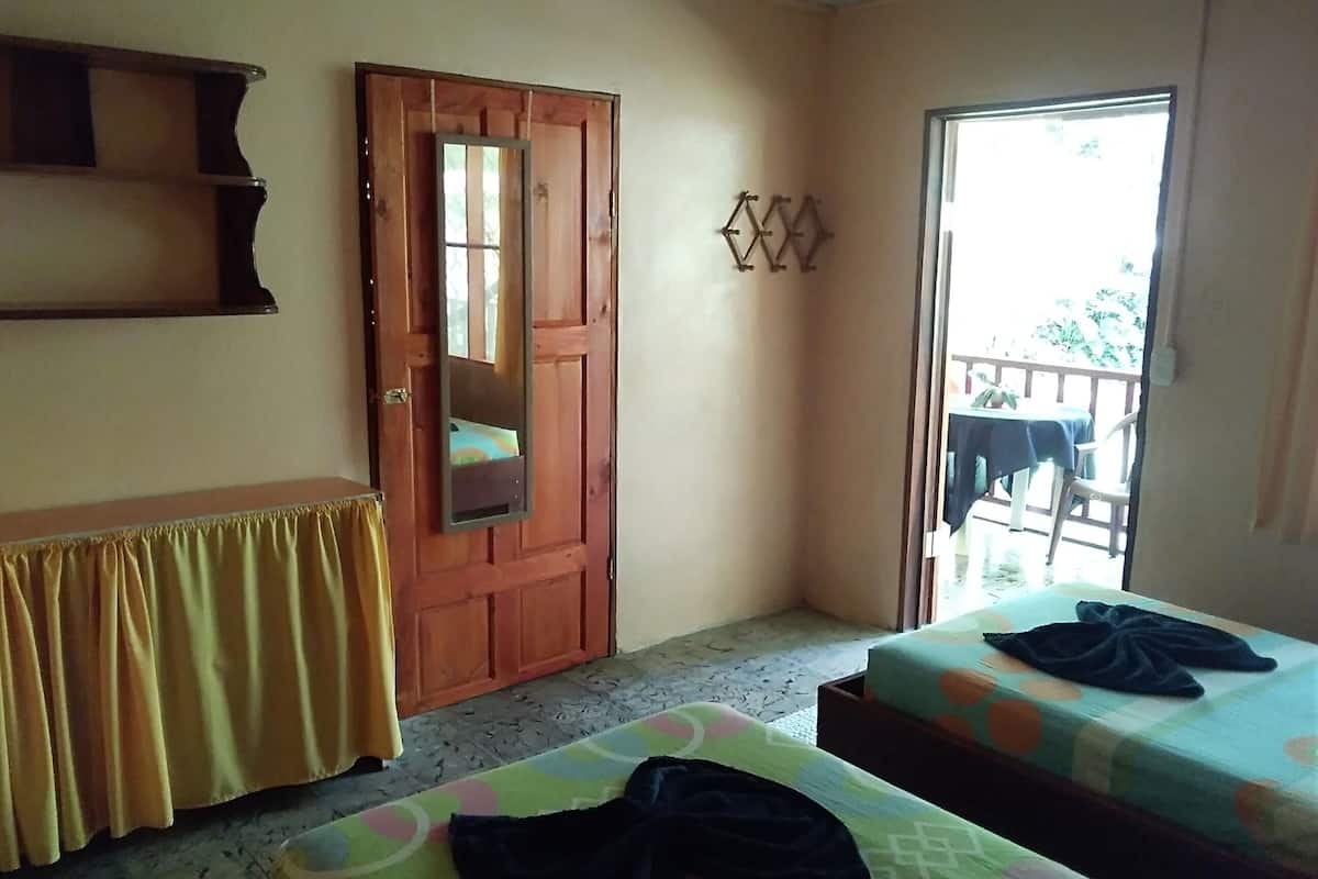 A room with two beds, a wooden door, a small table, and a balcony with a table and chairs.