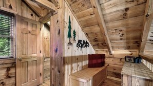 Ein Holzblockhaus-Innenraum mit einer Bank, einer Wand mit Baumdekorationen und einem Fenster mit Jalousien.
