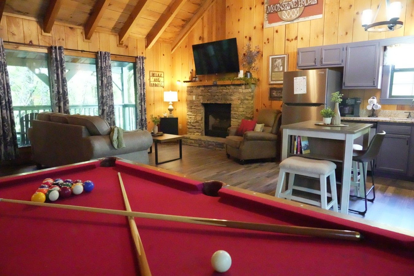 A pool table with balls, a sofa, a fireplace, a television, and a kitchen area.