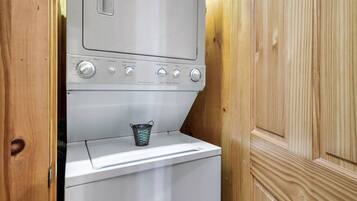 A compact laundry area with a washing machine and a drying machine, a metal bucket, and wooden paneling.