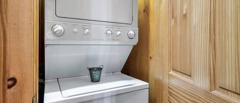 A compact laundry area with a washing machine and a drying machine, a metal bucket, and wooden paneling.