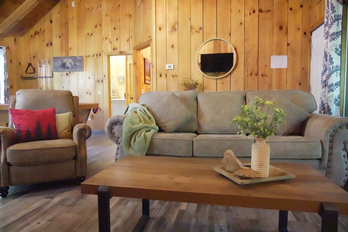 A wooden interior with a sofa, armchair, and a table with a plant.