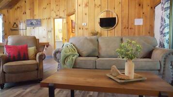 A wooden interior with a sofa, armchair, and a table with a plant.