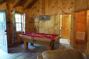 A pool table in a wooden room with a door and a window.
