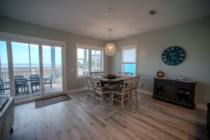 A dining area with a table and chairs, a chandelier, a clock, and a view of the ocean through large windows. - Upscale Beach Front Home w/Elevator, Private Pool, Fire Pit! (Cape San Blas)