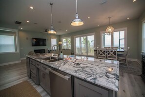 A spacious kitchen with a large island, pendant lighting, and a view to a deck area. - Upscale Beach Front Home w/Elevator, Private Pool, Fire Pit! (Cape San Blas)