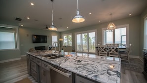 A spacious kitchen with a large island, pendant lighting, and a view to a deck area. - Upscale Beach Front Home w/Elevator, Private Pool, Fire Pit! (Cape San Blas)