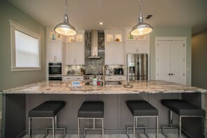 A modern kitchen with a large island, stainless steel appliances, and pendant lighting. - Upscale Beach Front Home w/Elevator, Private Pool, Fire Pit! (Cape San Blas)