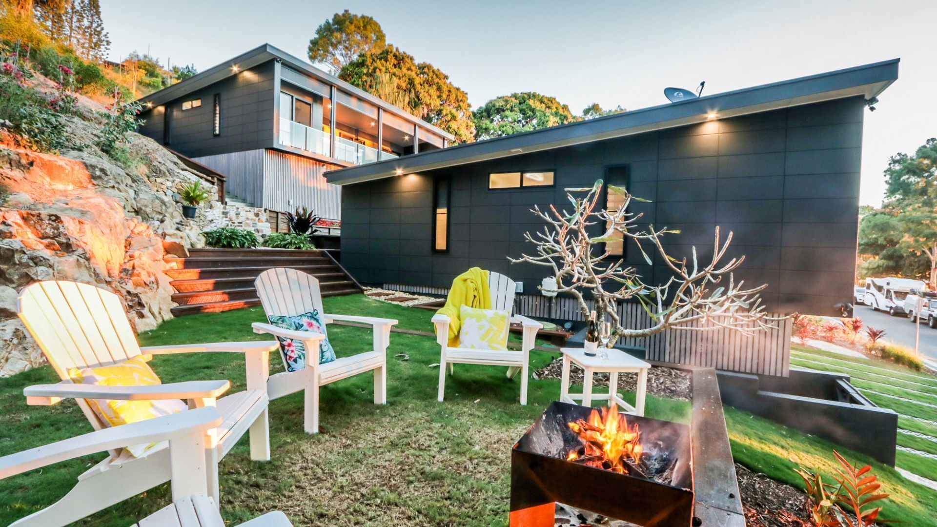 Une maison moderne dotée d’un foyer extérieur, d’un espace salon de jardin et offrant une vue sur le paysage environnant.