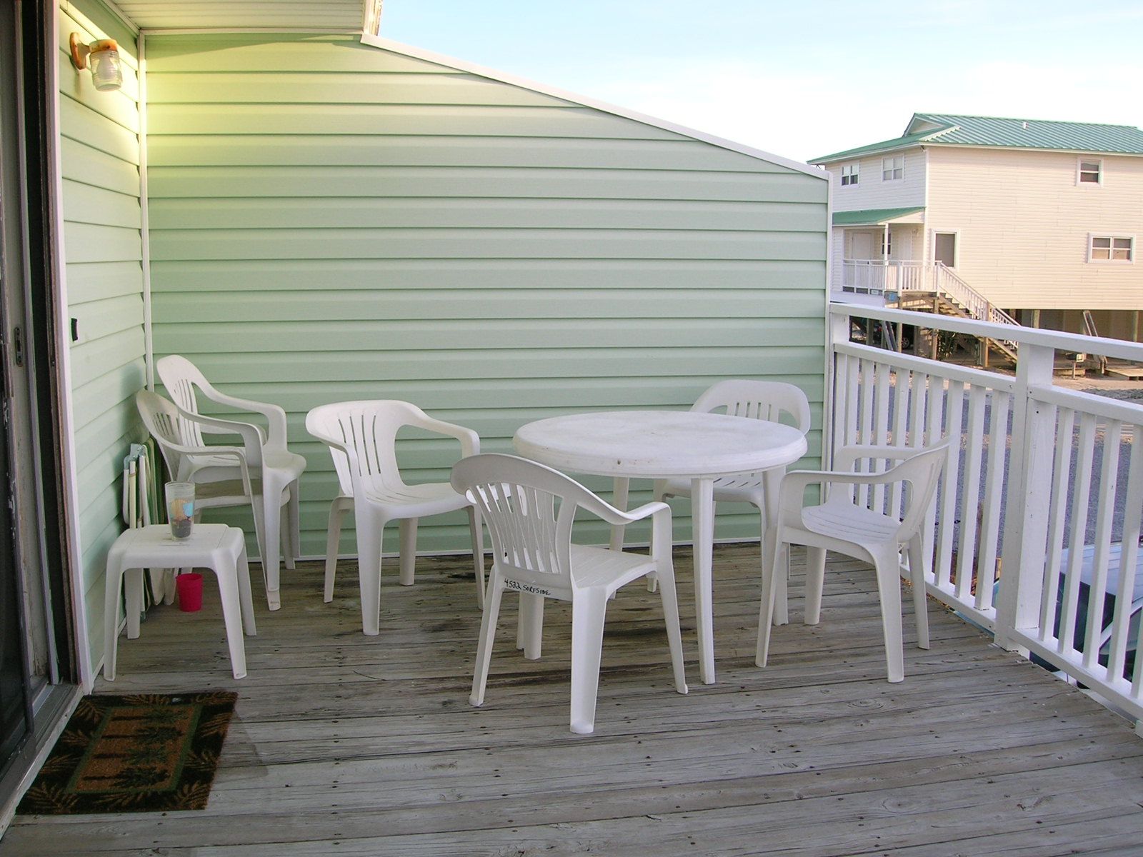 Een balkon met een witte tafel en stoelen, een rode emmer en een houten vloer.