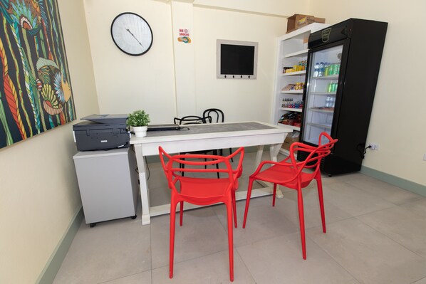 Una pequeña kitchenette con refrigerador, microondas y pileta. Hay dos sillas rojas y una mesa. Un reloj y un cartel de 'No Smoking' están en la pared.