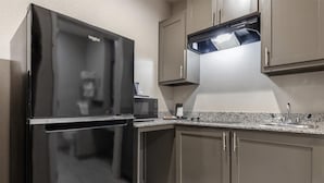 A modern kitchen with a black refrigerator, a microwave, a coffee maker, and granite countertops. - SureStay Plus Hotel by Best Western Ada (Ada)