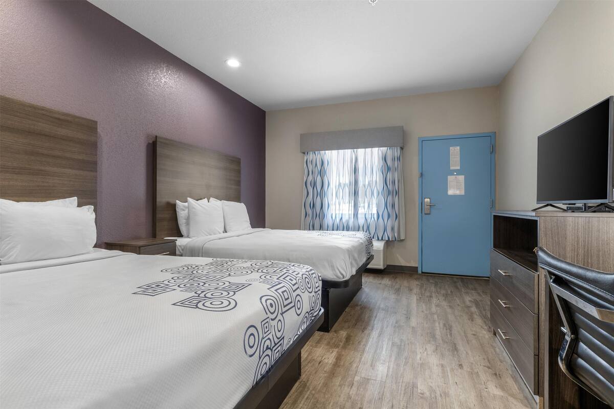 A hotel room with two beds, a TV, a wardrobe, and a window with curtains.