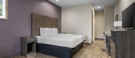 A modern hotel room with a bed, bedside table, TV, and a desk with a chair.