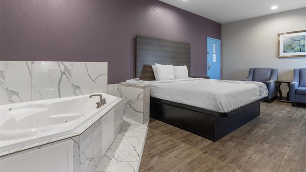 A modern bedroom with a large bed, a separate bathroom with a bathtub, and a small seating area. - SureStay Plus Hotel by Best Western Ada (Ada)
