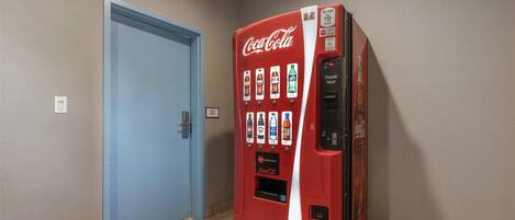 A Coca-Cola vending machine in a hallway with a blue door and beige walls.
