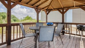 A covered outdoor patio with a wooden deck, metal chairs, and a barbecue grill. - SureStay Plus Hotel by Best Western Ada (Ada)