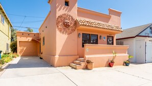 Une maison à deux étages avec un garage, une petite tourelle ornée d’un soleil décoratif sur la façade, et des plantes en pot à l’entrée.