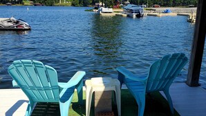 Un muelle con dos sillas Adirondack azules, una mesita blanca y un taburete de ladrillo.