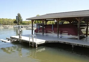 A covered boat launch ramp with a metal ladder, a dock extending into a body of water, and a building with a red roof in the background. - GO JUMP IN THE LAKE at this lovely waterfront home! (Mineral)