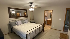 Een slaapkamer met een bed, een plafondventilator, een spiegel en een deur naar een badkamer.