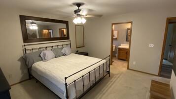 A bedroom with a bed, a ceiling fan, a mirror, and a door leading to a bathroom.