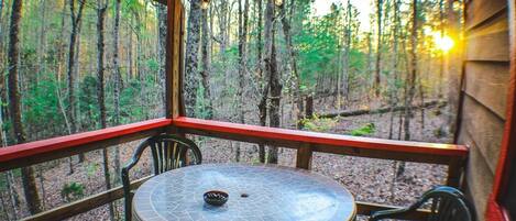 Enjoy a serene forest view from this deck with a round table and two chairs.