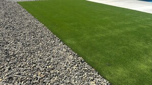 Ett välplanerat utomhusområde med konstgräs, en betongterrass och utsikt över avlägsna berg.