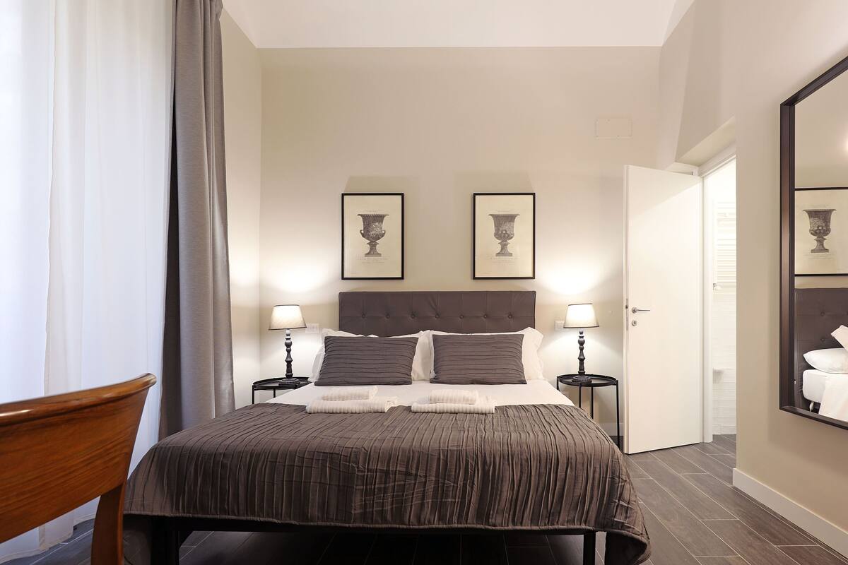A neatly made bed with a brown bedspread, two bedside lamps, and two framed pictures on the wall.