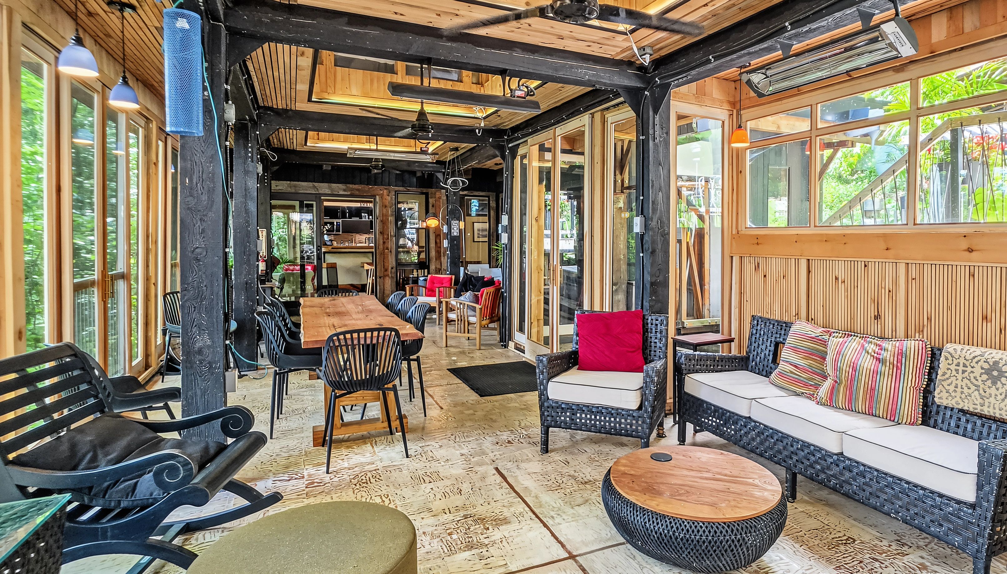 A wooden interior with a dining area, seating, and a view through large windows.