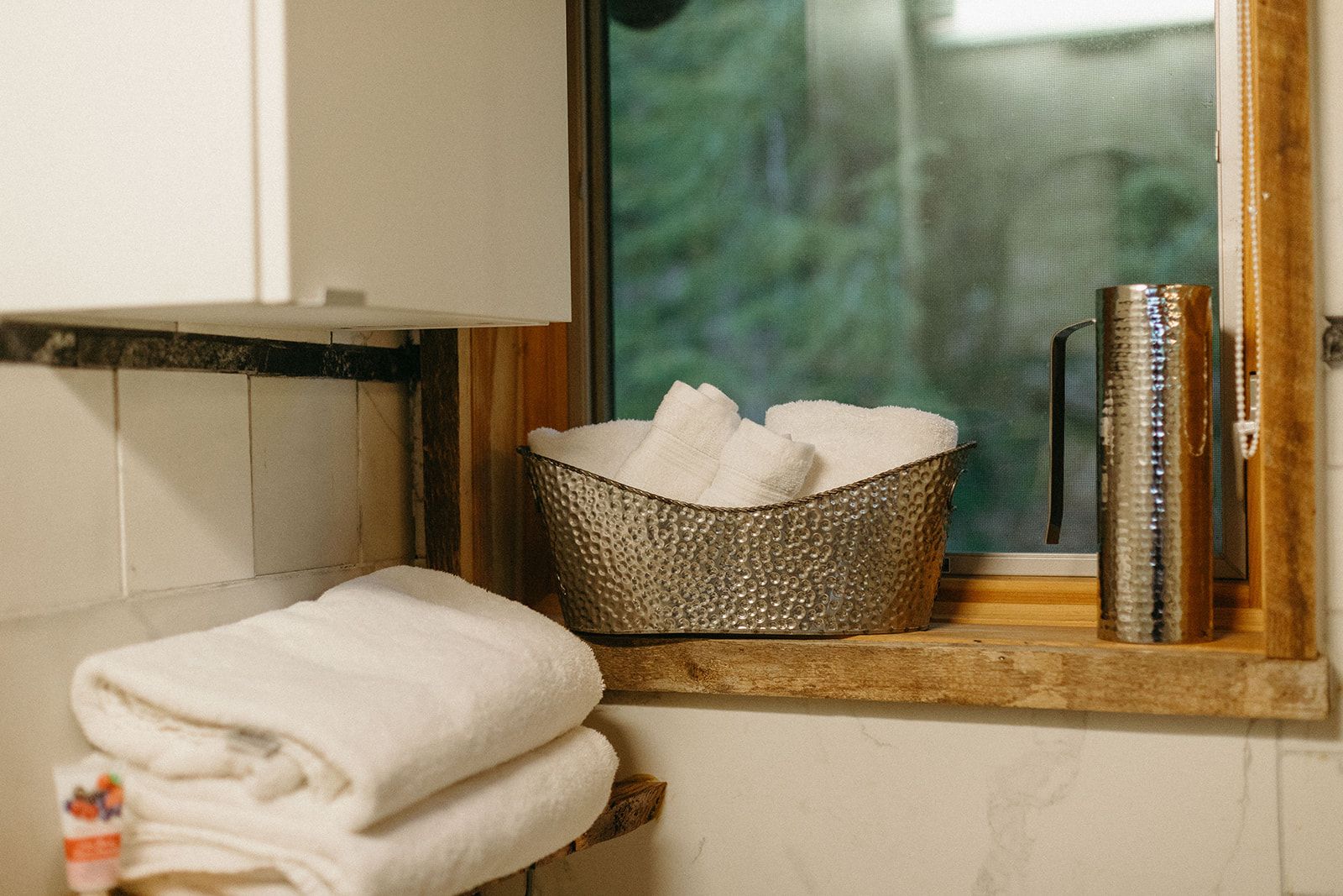 Une salle de bain avec une fenêtre, un panier en métal contenant des serviettes et une étagère en bois.