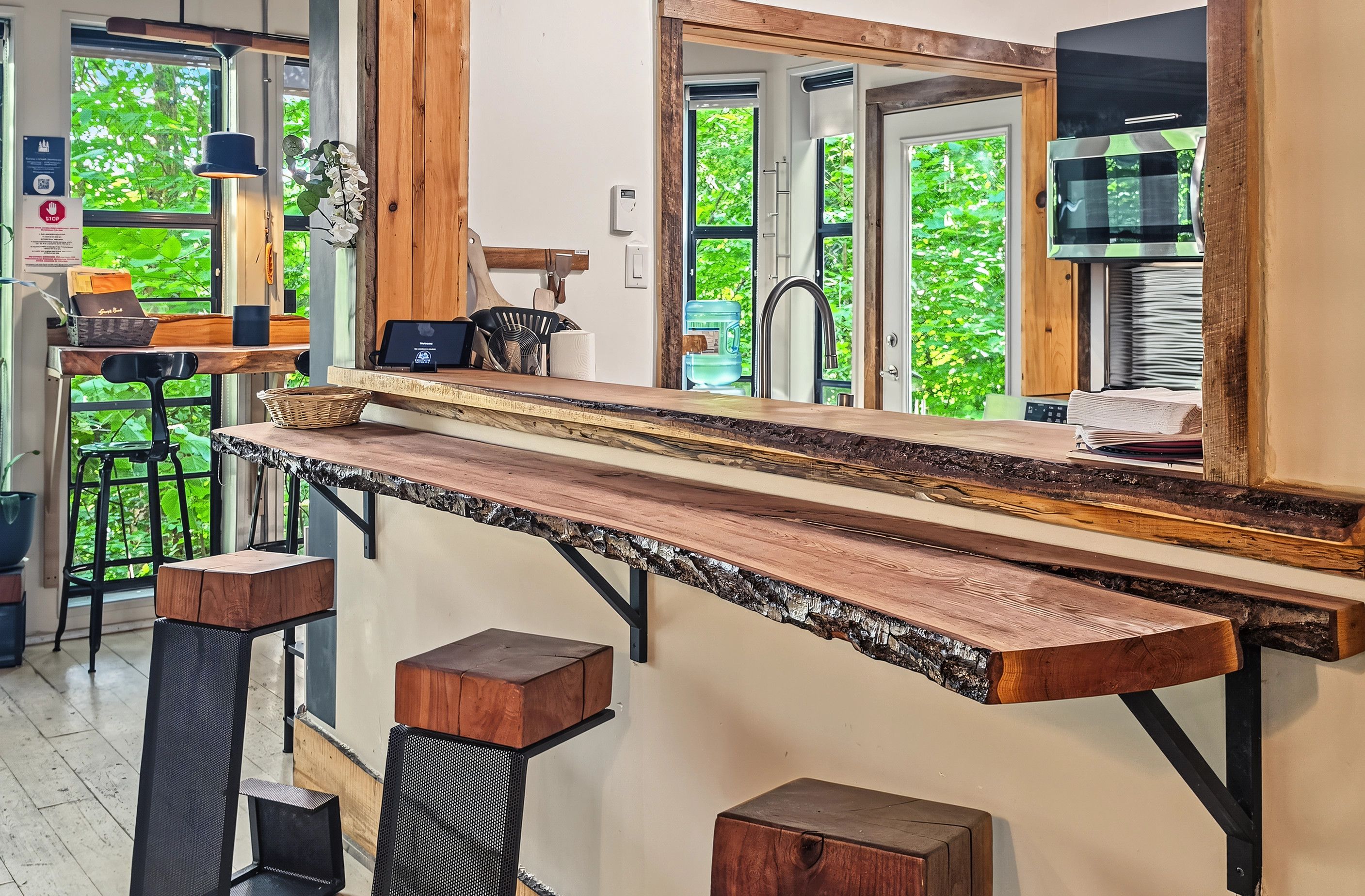 A kitchen area with a long wooden countertop, stools, and a view of greenery outside.