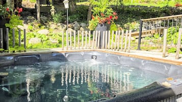 A hot tub surrounded by a wooden fence, with a garden and a wooden deck in the background.