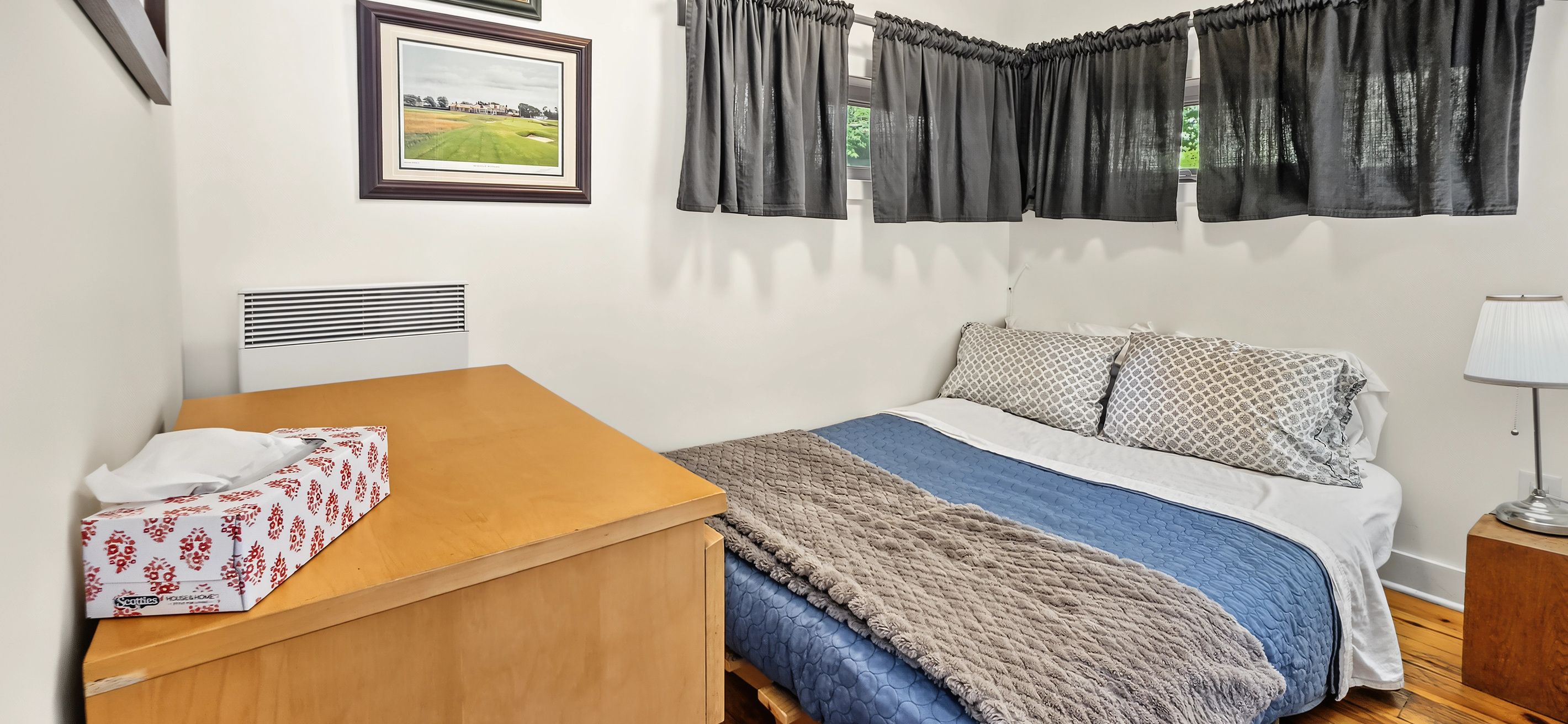 A bedroom with a bed, a wooden nightstand, a framed picture on the wall, and a window with curtains.