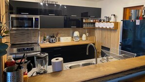 Een moderne keuken met zwarte kastjes, een roestvrijstalen magnetron, een koffiezetapparaat en een koelkast.