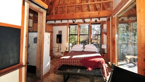 A wooden-framed bedroom with a bed, a window, and a door leading to a bathroom.