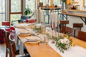 A dining table set with plates, glasses, and candles, surrounded by chairs and a view of the outdoors.