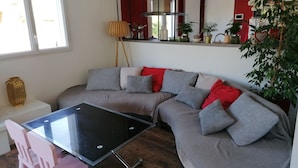 Una sala moderna con un sofá seccional, una mesa de vidrio y un comedor con sillas rosadas.