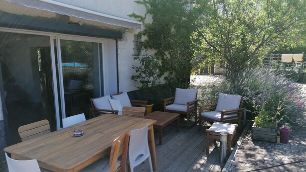 Un patio al aire libre con una mesa y sillas de madera, una puerta corrediza de vidrio y plantas en macetas.