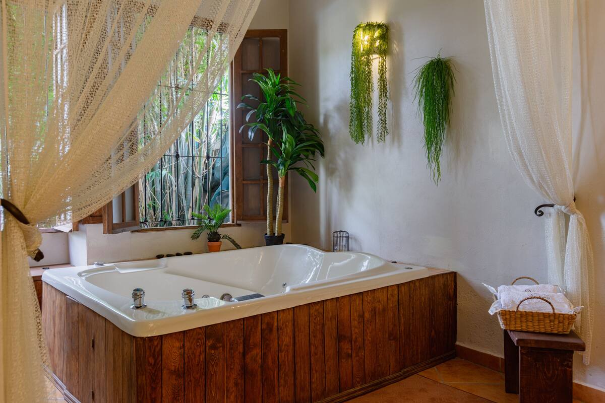 Un baño con una bañera de madera, una planta en maceta y una planta colgante en la pared.