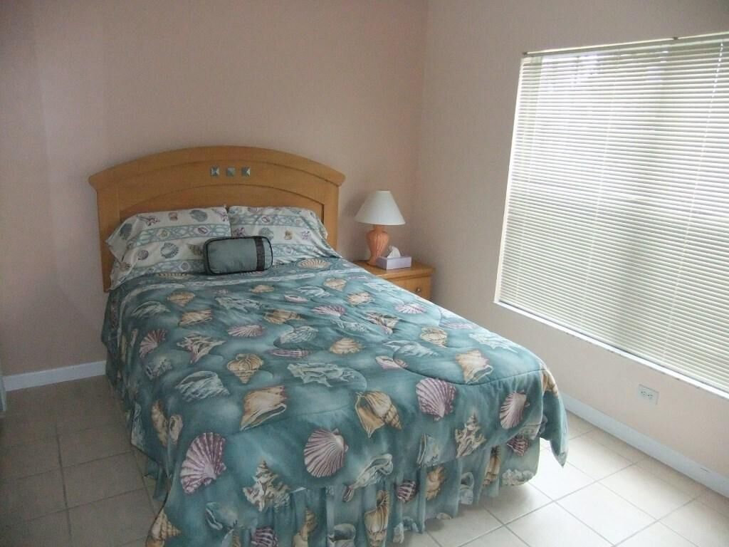 A bedroom with a bed, a nightstand, a lamp, and a window with blinds.