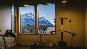 Un gimnasio con equipo de ejercicio, una cinta de correr y vistas a las montañas a través de amplios ventanales.