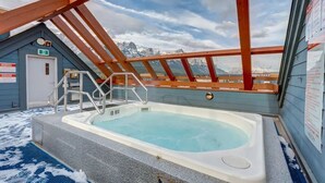 Un jacuzzi con vistas a montañas, una terraza de madera y una puerta con un letrero.