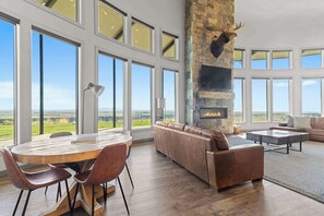 A spacious living room with a stone fireplace, leather sofas, and large windows offering a view of the countryside.