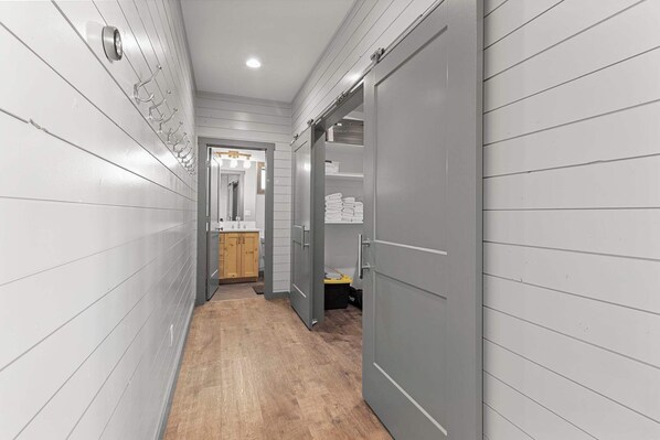 A narrow hallway with wooden paneling, a wooden floor, and a door leading to a bathroom with a toilet and sink.