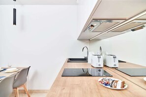 Uma cozinha moderna com uma mesa de jantar, um fogão por indução preto, uma chaleira, duas torradeiras brancas e um prato de petiscos.