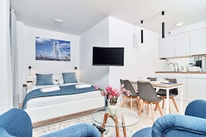 Una habitación de hotel moderna con cama, televisor, zona de comedor y cocina.